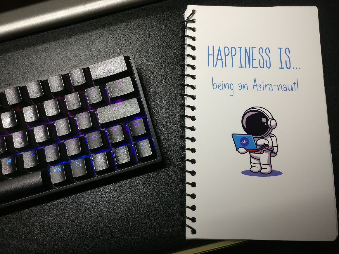 A notebook with a cartoon astronaut holding a laptop and the following words on the cover: "Happiness is... being an Astra-naut!"